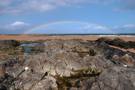 a rocky beach on a warm wet day with a calm sea and a rainbow after a shower an ideal place to have a walk in ireland