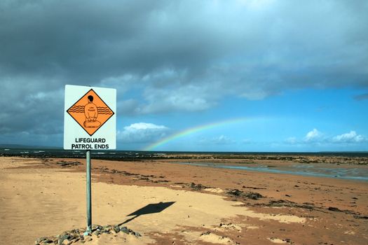 a sign warning that there is no lifeguard patrol beyond this sign with a beautiful rainbow in the background