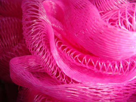 A close up photo of a bright pink bath wash puff.