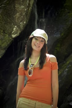 A young woman posing in front of a nice waterfall in the woods.