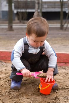 Child sitting in sandbox on cold spring day