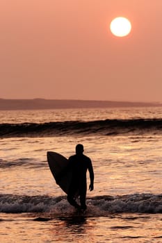 Surfer exiting the water. Silhouette of man carrying surfboard