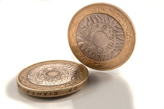Close and low level capturing a selection of British two pound coins arranged over white.