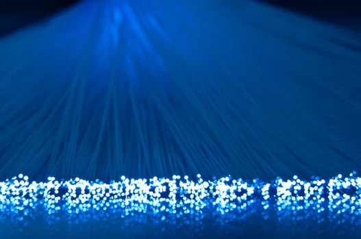 Close and low level capturing the ends of many illuminated blue fibre optic strands and their foreground reflections.