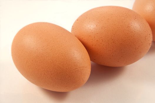 Close up and low level angle of several fresh brown eggs arranged over white.