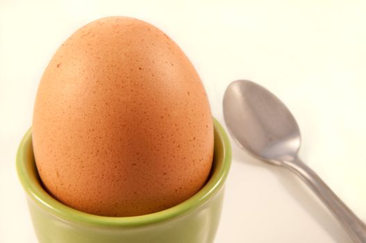 Close up of a boiled egg arranged in a lime green ceramic eggcup with white background and silver spoon.