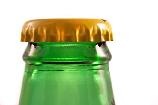 Close up and low level capturing the top of a green glass bottle neck with sealed yellow metal bottle cap in place. White background.