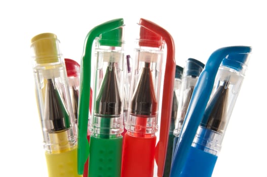 Close up and low level angle capturing the tops of a group of coloured pens arranged vertically with white background.