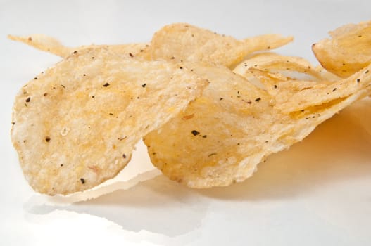 Close up of a group of potato crisps arranged on a white reflective surface with white background.