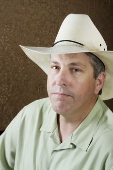 Man wearing a white cowboy hat in front of a gold background
