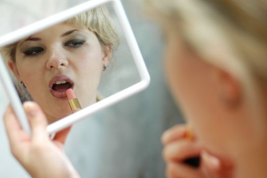 A beautiful young woman applying her make-up in the mirror