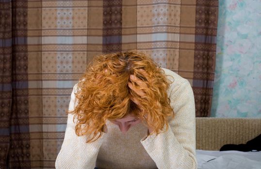 Young stressed woman sitting on the bed and hold her hand on her own head