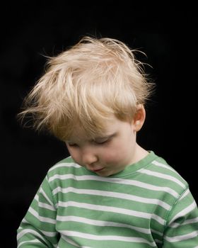 Sad little boy on black background. Boy have blond hair and a bit of dirt on face