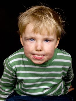 Little boy making funny face on black background. Boy have blue eyes and blond hair and have a bit of dirt on his face