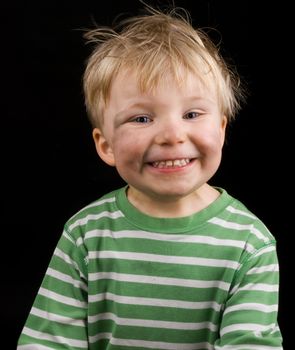 Smiling little boy on black background. Boy have blue eyes, blond hair and a bit of dirt on his face