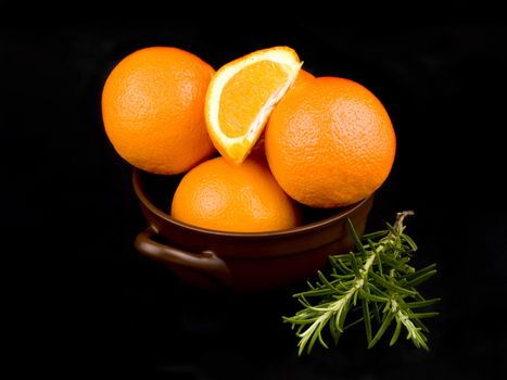 Few oranges in ceramic bowl on black background