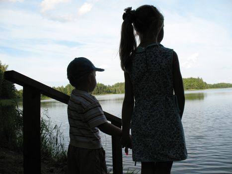 Small brother and sister silhouette on a lake.