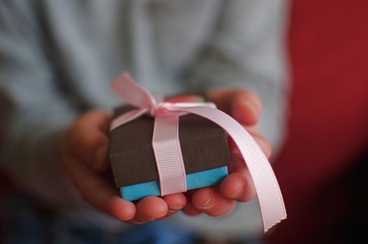 A little boy holds out a tiny package for a birthday or Christmas.  Shallow depth of field and lots of color.