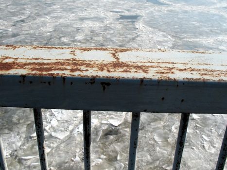 Rusty railing over frozen river.