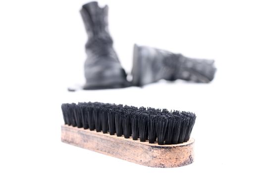 Brush used for shoeshining and black boots in the background. isolated on white background