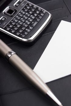 Closeup of cellphone, businesscard and pen in a black leather folder.