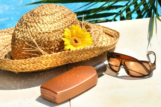 Straw hat, glasses and suntan lotion by the pool