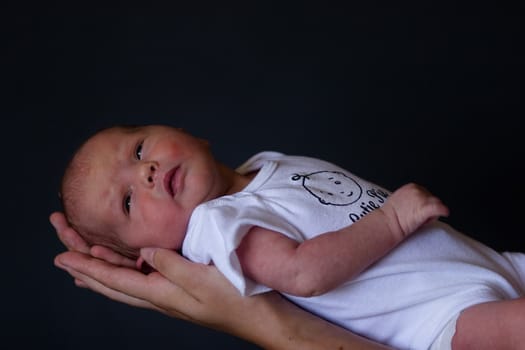 Little 7 days old baby lying securely on mom's arms, against a black background