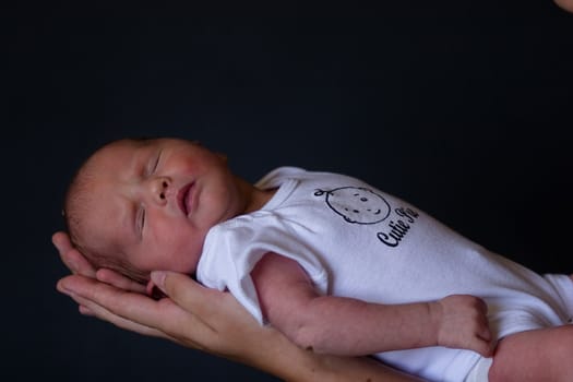 Little 7 days old baby lying securely on mom's arms, against a black background