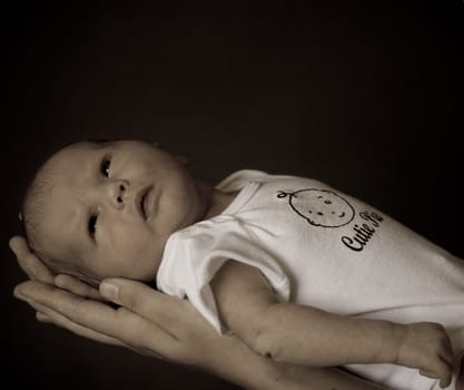 Little 7 days old baby lying securely on mom's arms, against a black background