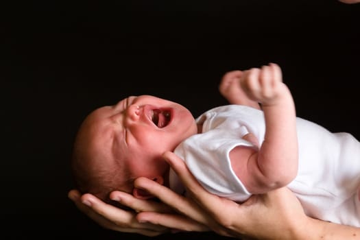 Little 7 days old baby lying securely on mom's arms, against a black background