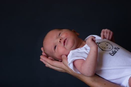Little 7 days old baby lying securely on mom's arms, against a black background