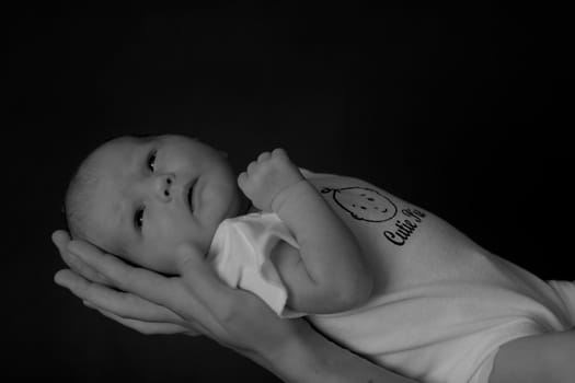 Little 7 days old baby lying securely on mom's arms, against a black background