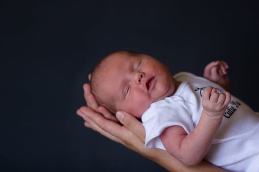 Little 7 days old baby lying securely on mom's arms, against a black background