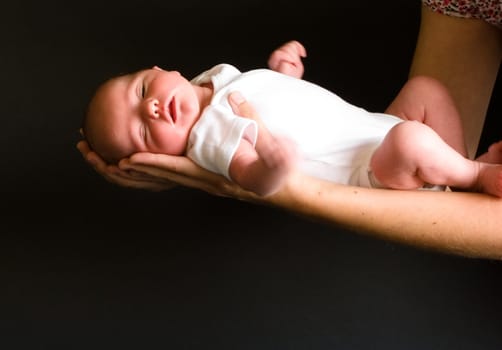 Little 7 days old baby lying securely on mom's arms, against a black background