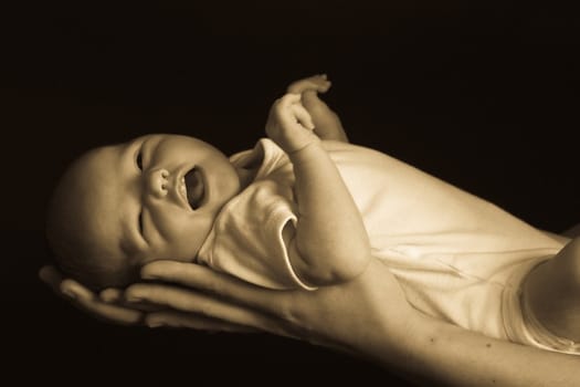 Little 7 days old baby lying securely on mom's arms, against a black background