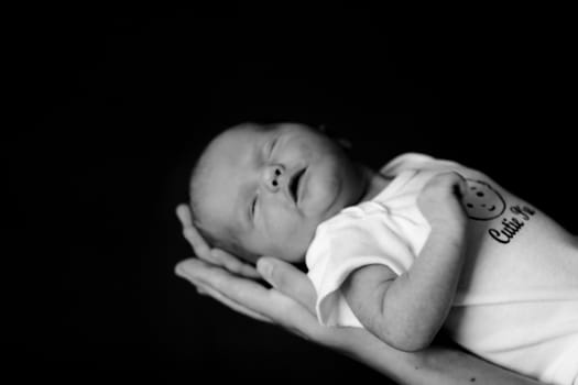 Little 7 days old baby lying securely on mom's arms, against a black background