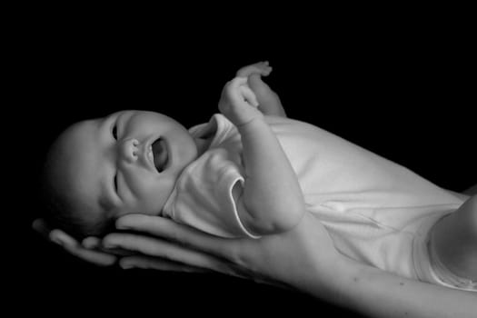 Little 7 days old baby lying securely on mom's arms, against a black background