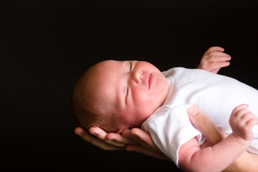 Little 7 days old baby lying securely on mom's arms, against a black background