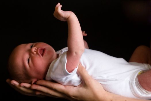 Little 7 days old baby lying securely on mom's arms, against a black background