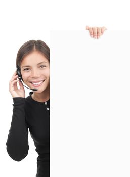 Call center woman with headset holding blank white billboard sign. Smiling and friendly young mixed race chinese / caucasian secretary or telemarketing assistant isolated on white background.