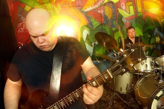 Heavy rock band playing. Shot with strobes and slow shutter speed to create lighting atmosphere and blur effects.  Slight movement visible on both players.
