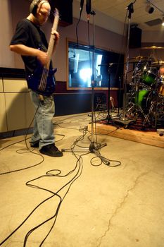 A bass player recording his tracks in a recording studio with natural outside light streaming into the control room.  Slow shutter speed with ambient light - bass player has motion blur from slow shutter.
