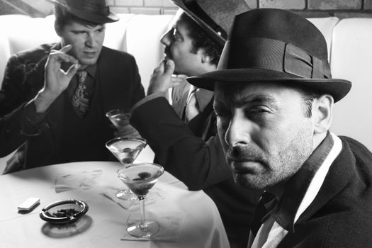 Three Caucasian prime adult males in retro suits sitting at table.