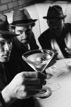 Three Caucasian prime adult males in retro suits sitting at table with martini.