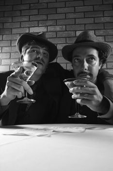 Two Caucasian prime adult males in retro suits sitting at table with martinis.