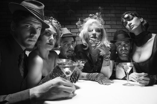 Group of Caucasian prime adult retro males and females sitting at table in lounge looking at viewer.