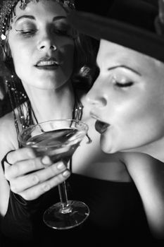 Caucasian prime adult retro female taking drink of girl friend's martini.