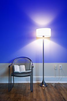 Blue projection light on wall with bright floor lamp and open book on chair.