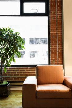 Cushy chair in loft apartment with houseplant in front of window.