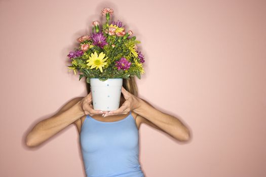 Caucasian mid-adult female holding pot of flowers in front of her face.